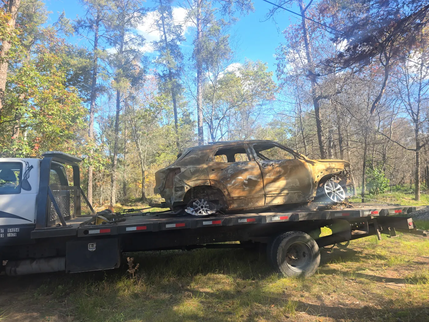 Burned-out SUV recovered and secured on a C&C Inc flatbed tow truck in the Northern Michigan woods
