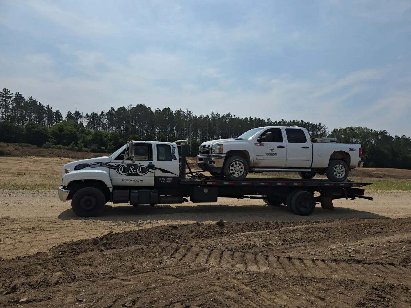 C&C Inc flatbed tow truck from Roscommon, MI hauling a white Chevy Silverado 2500HD pickup