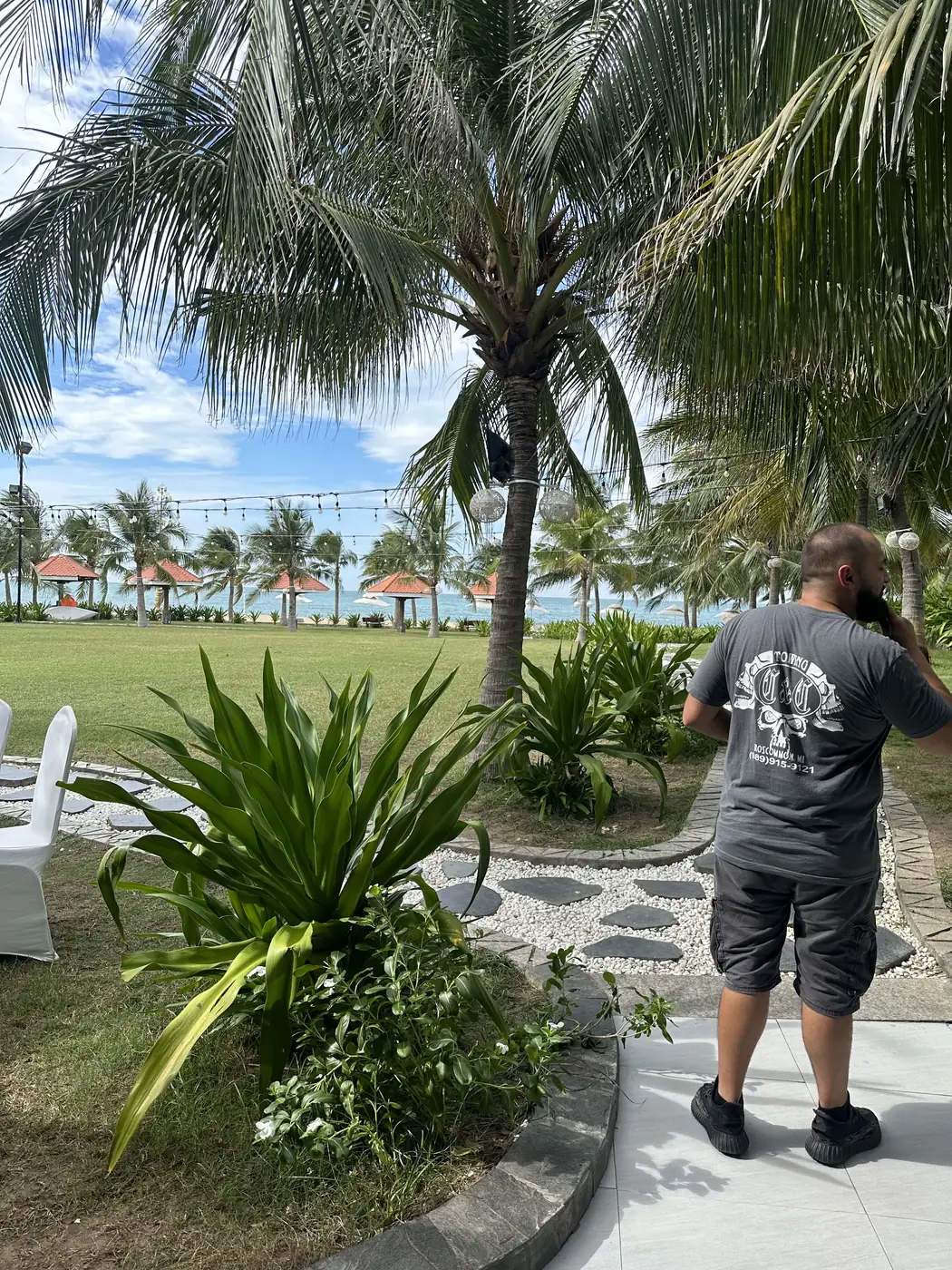 Wearing a gray C&C Towing shirt at a tropical beach resort under the palm trees